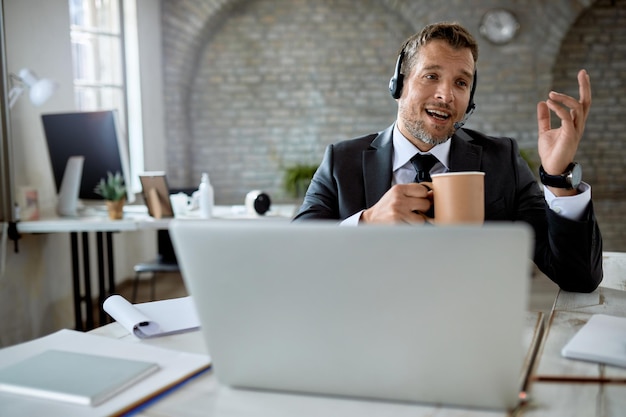 Empresário masculino tomando café enquanto faz videochamada no computador no escritório