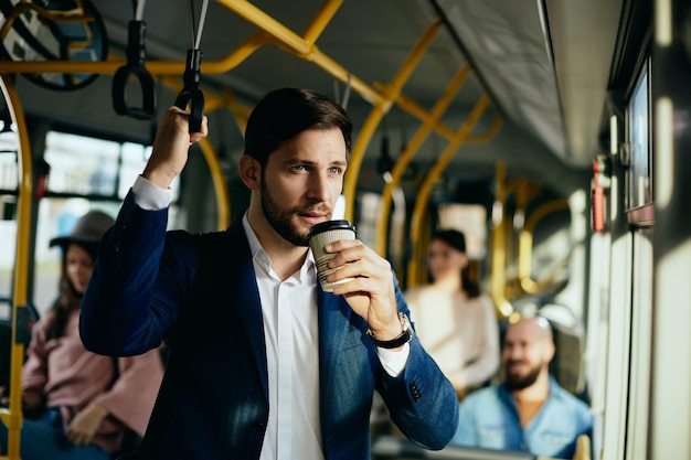 Empresario masculino tomando café para llevar mientras viaja al trabajo en autobús