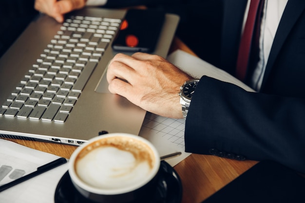 Empresário masculino usando laptop no café. Caderno e xícara de café fecham.