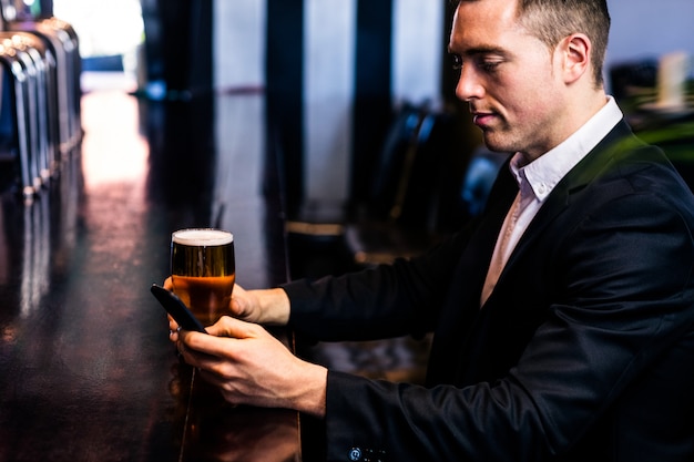 Empresario mensajes de texto y tomando una cerveza en un bar