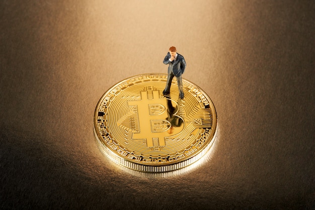 Empresario en miniatura de pie sobre un Bitcoin