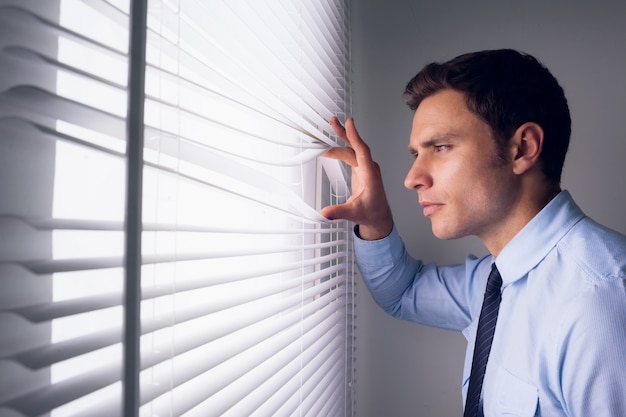 Empresario mirando a través de las persianas en la oficina