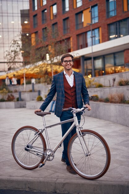 Empresário moderno e alegre com bicicleta na calçada