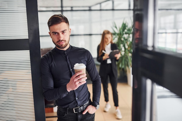 Empresário moderno em pé dentro de casa no escritório. sua colega atrás.