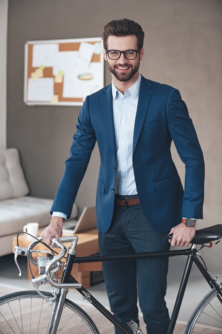 Foto empresário moderno. jovem bonito usando óculos e terno olhando para a câmera com um sorriso em pé com uma bicicleta retrô no escritório