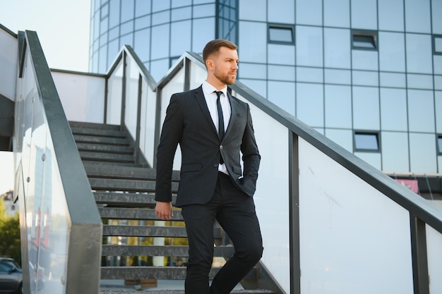 Empresário moderno Jovem confiante de terno completo e olhando para longe enquanto está ao ar livre com a paisagem urbana ao fundo