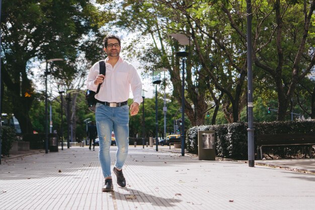 Empresario moderno latino de mediana edad con una sonrisa y una mochila caminando por un sendero Copiar espacio