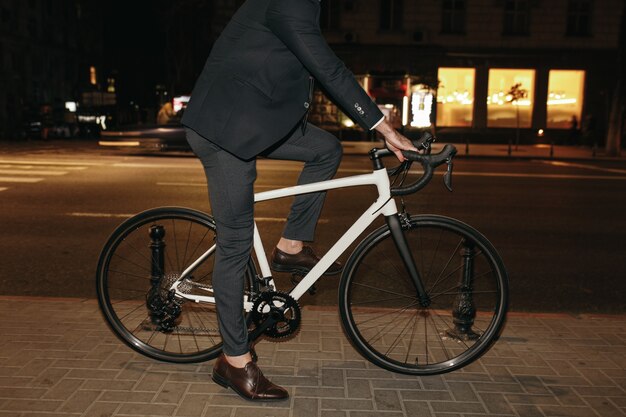 Empresario moderno en traje montando bicicleta en la ciudad de noche