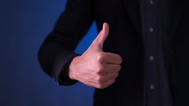 Empresário mostrando o sinal OK com o polegar acima no fundo azul e preto.