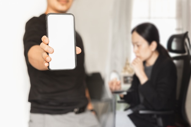 Empresario mostrando teléfono móvil con pantalla en blanco mientras la mujer trabaja en segundo plano.