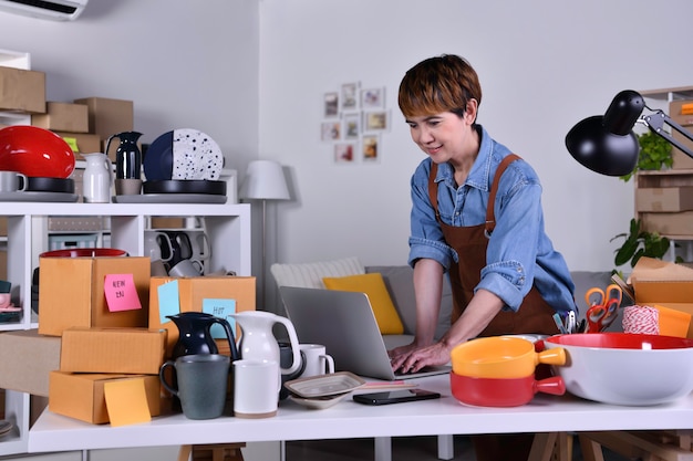 Empresario de mujer asiática madura, propietario de un negocio que trabaja en una computadora portátil, verificando la dirección y los detalles de la entrega antes de enviar el producto. Trabajo de negocios de venta en línea en concepto de hogar