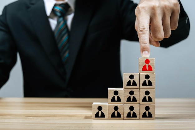 Foto empresário na mão de terno preto escolhendo no ícone humano vermelho no bloco de cubo de madeira no topo pirâmide pilha liderança líder da equipe de gerenciamento de negócios estratégia de negócios conceito de gerenciamento de recursos humanos