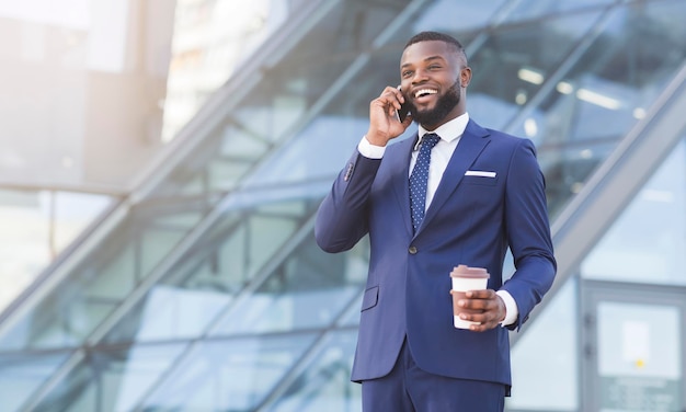 Empresário negro falando ao telefone segurando a xícara de café na cidade