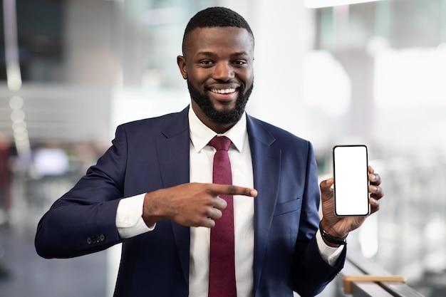 Empresario negro positivo apuntando al teléfono inteligente con pantalla vacía