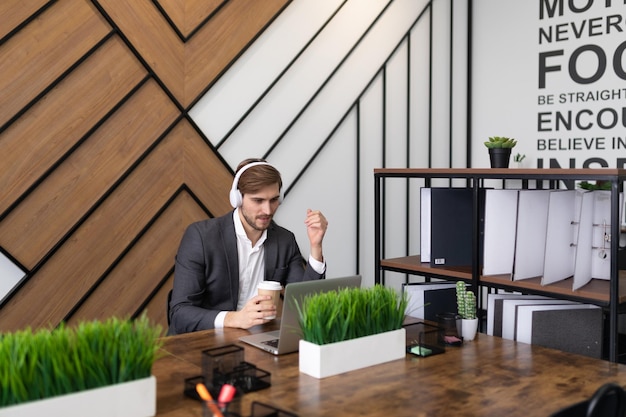 Empresário no escritório em um laptop em fones de ouvido assistindo a um webinar
