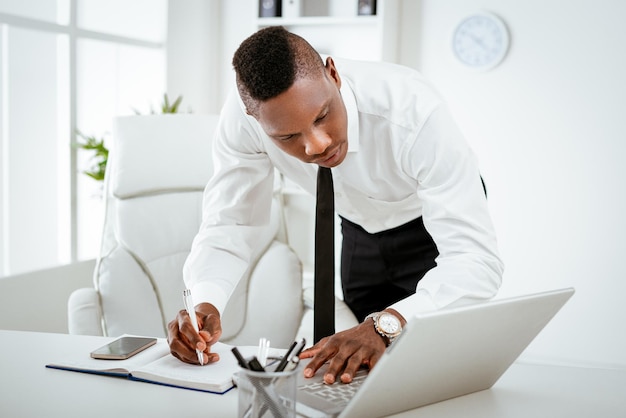Empresário ocupado africano trabalhando no escritório. Ele está de pé e usando laptop.