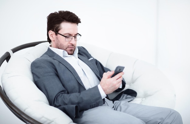 Empresário olha para a tela do smartphone sentado em uma cadeira confortável