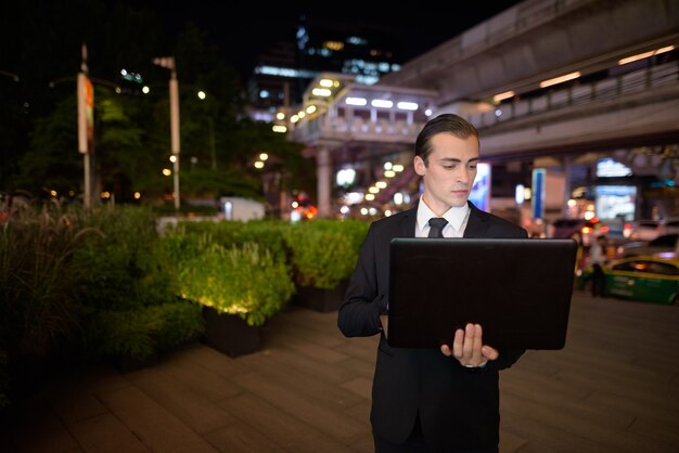 Empresario con ordenador portátil al aire libre por la noche en la ciudad