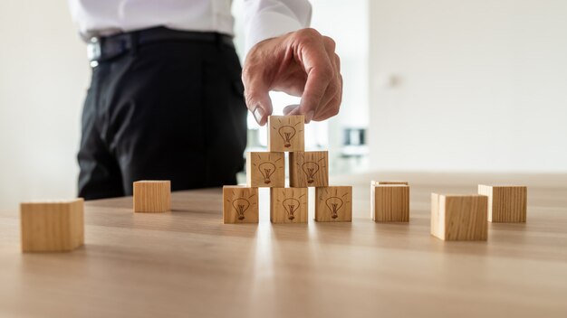 Empresário organizando cubos de madeira com ícones de lâmpada na mesa do escritório