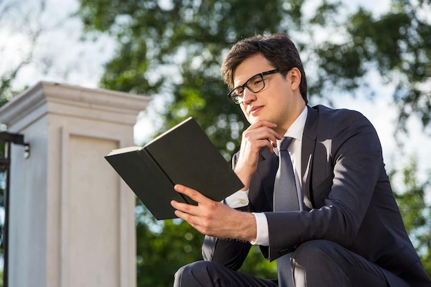 Empresário pensativo lendo livro lá fora