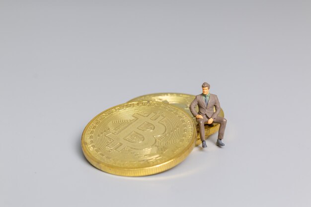 Empresario de personas en miniatura sentado en monedas Bitcoin