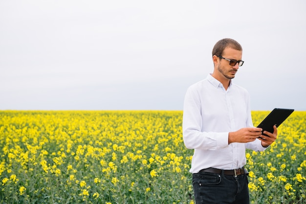 empresario de pie en el campo de colza con tableta