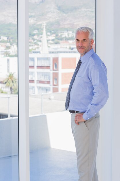 Empresario de pie junto a la ventana y sonriendo