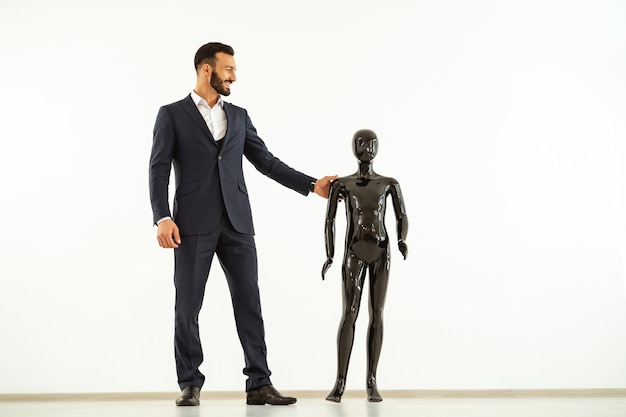 El empresario de pie con un maniquí negro sobre fondo blanco.