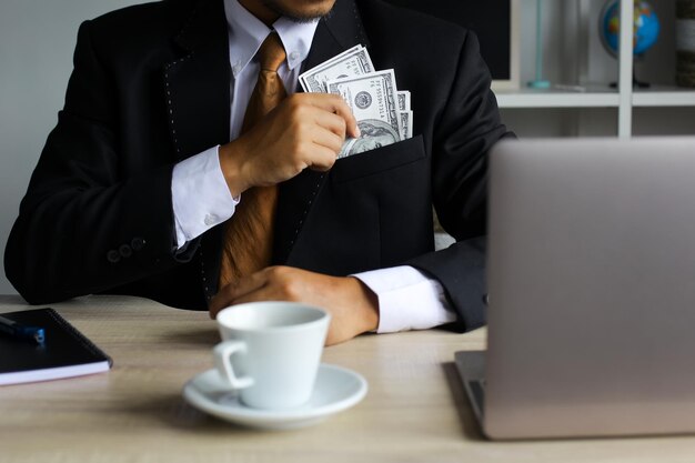 Empresario poniendo billetes de dólar en su bolsillo en la oficina