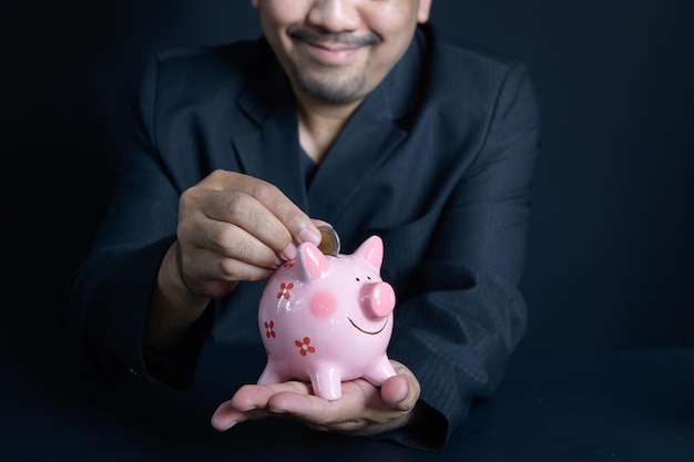 Empresario poniendo moneda de dinero en piggy para ahorrar dinero y riqueza financiera