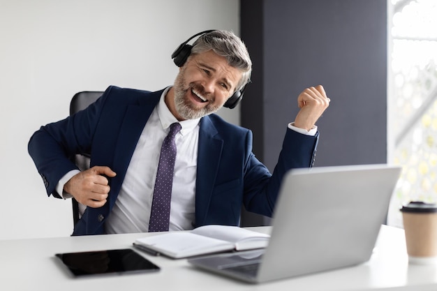 Empresario positivo de mediana edad escuchando música en auriculares y tocando guitarra virtual