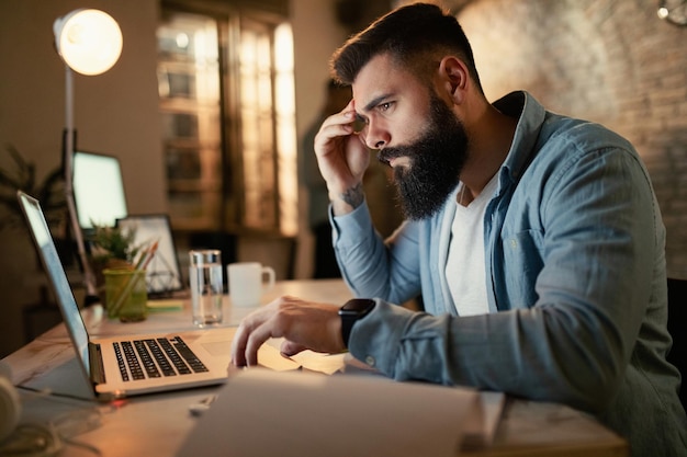 Empresario preocupado leyendo un correo electrónico en una computadora mientras trabaja de noche en la oficina