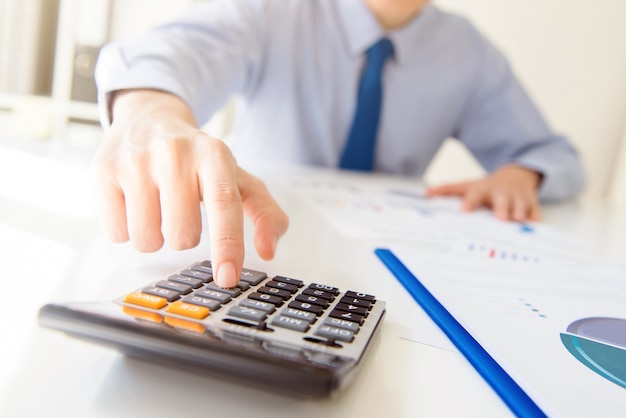 Empresario presionando el botón de la calculadora en la mesa de trabajo en la oficina