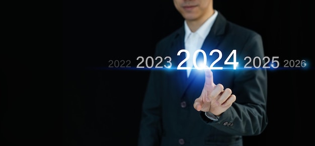 Foto empresario presionando y señalando con el dedo el año 2024 en una pantalla virtual sobre un fondo oscuro planificación de negocios objetivos y logros en 2024 concepto de feliz año nuevo copiar espacio