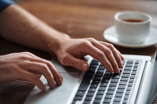 Empresário pressionando um dos botões do teclado do laptop enquanto se conecta ou organiza o trabalho na mesa