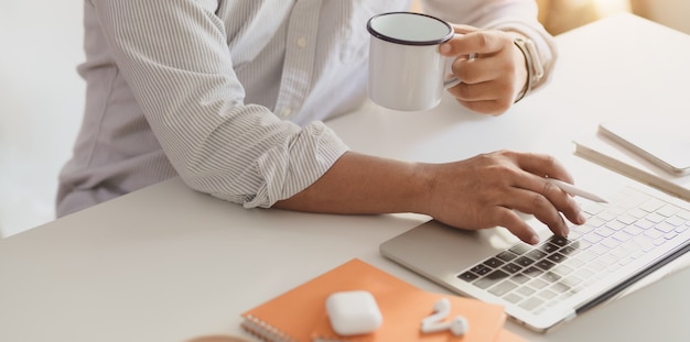 Empresário profissional digitando no computador portátil enquanto bebe uma xícara de café