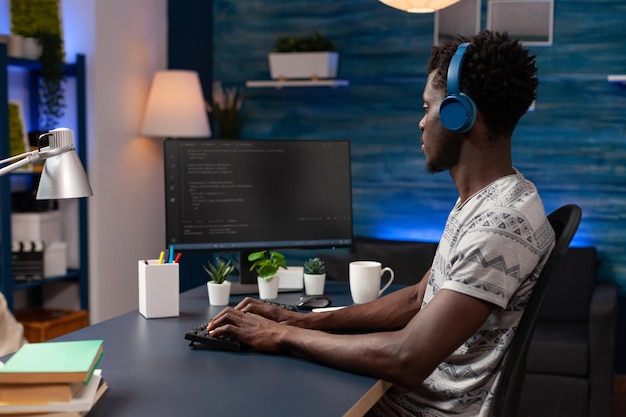 Empresario programador con auriculares escribiendo código binario para la seguridad del sitio web trabajando de forma remota desde casa. Desarrollador de ti afroamericano escribiendo infografías javascript programando servidor de firewall