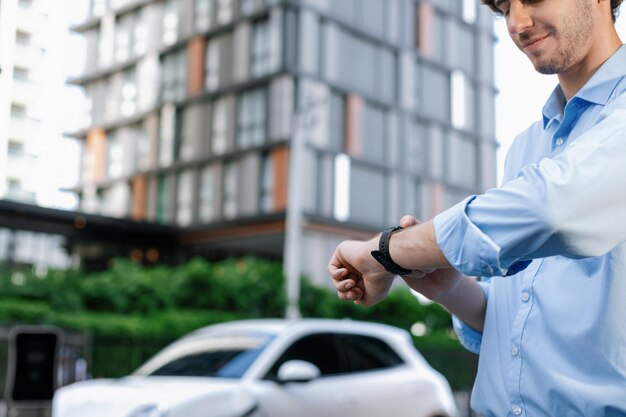 Empresario progresista con reloj inteligente en la estación de carga pública para automóviles EV