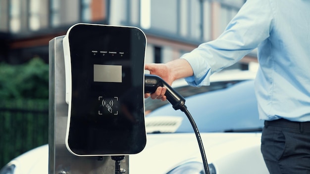 Empresário progressista instala um plugue de carregador da estação de carregamento no seu carro elétrico antes de dirigir pelo centro da cidade um carro recarregável ecológico alimentado por energia sustentável e limpa