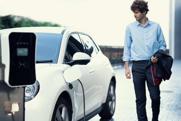 Empresário progressivo com carro ev na estação de carregamento de carros de estacionamento público