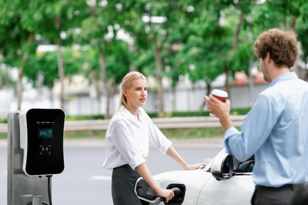 Empresário progressivo e empresária no ponto de carregamento e carro EV