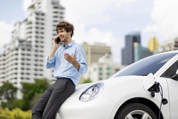 Empresário progressivo falando ao telefone com recarga de veículo elétrico