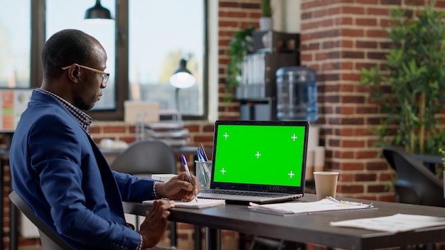 Empresario que trabaja con una pantalla verde en una computadora portátil, planificando un proyecto con una plantilla de clave de croma en blanco y un espacio de copia de maqueta aislado. Empleado mirando el fondo de la computadora.