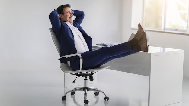 Empresario relajado con una sonrisa radiante apoyado en su silla con las piernas en el escritorio