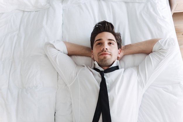 Empresario relajado vistiendo ropa formal acostado en la cama en el apartamento del hotel