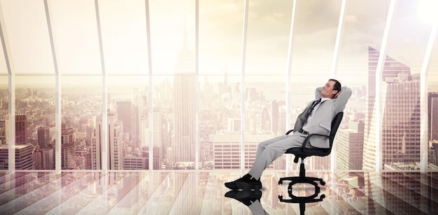 Empresário relaxando em cadeira giratória contra sala com grande janela olhando para a cidade