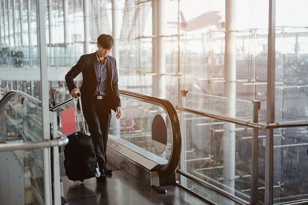 Empresário se movendo para o portão do terminal pela escada rolante para check-in, embarque com bagagem no aeroporto.