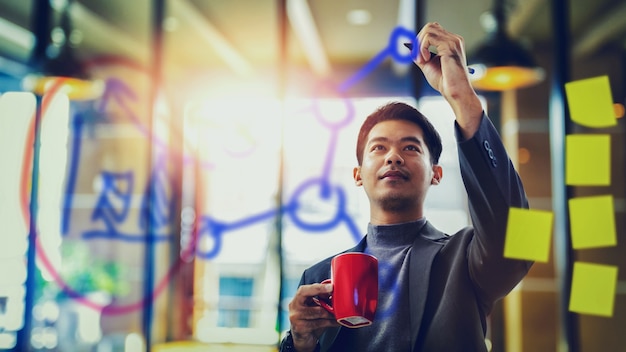 Empresário segurando a caneca de café e escrever dados na placa transparente