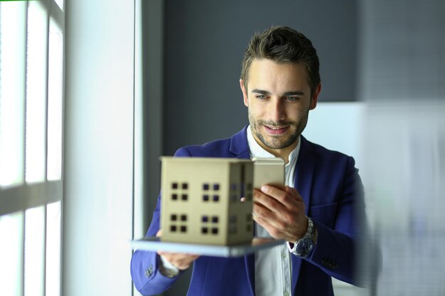 Foto empresário segurando a miniatura da casa na mão em pé no escritório