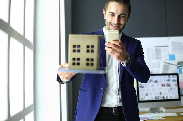 Empresário segurando a miniatura da casa na mão em pé no escritório